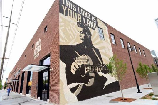 A mural of Woody Guthrie with the title of his most famous song emblazoned across the top guides visitors to the Woody Guthrie Center in downtown Tulsa